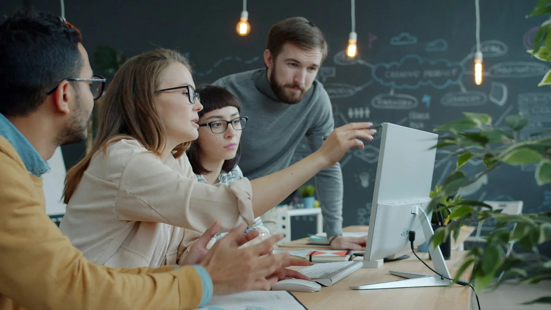 Four colleagues reviewing something together on a desktop monitor in an open workspace