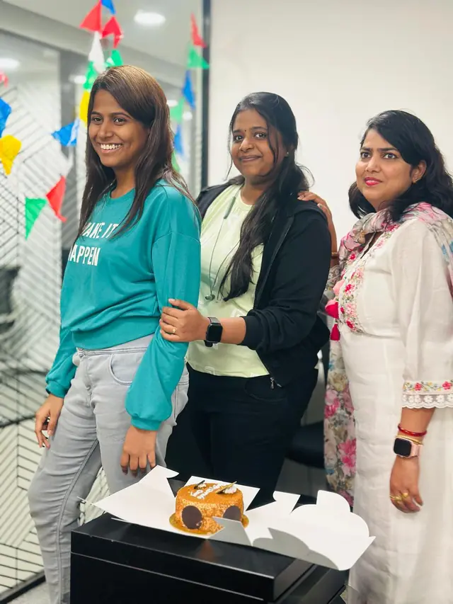 Three colleagues smiling beside a cake under colourful bunting for Women's Day