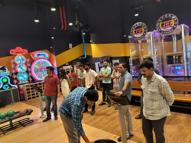 Colleagues watching a teammate bowl at a bowling alley lit by arcade machines