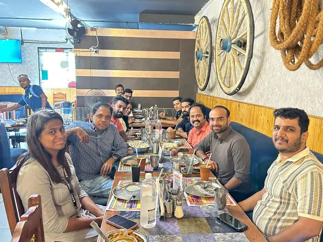 Colleagues around a long restaurant table set with thali plates, old cart wheels on the wall behind them