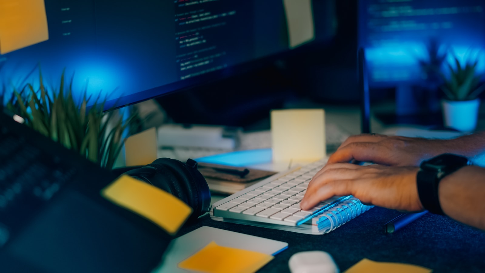 Hands at a keyboard in a dim office, source code and notes on the desk