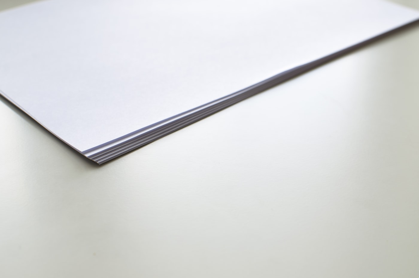 A neat stack of blank white paper on a pale desk