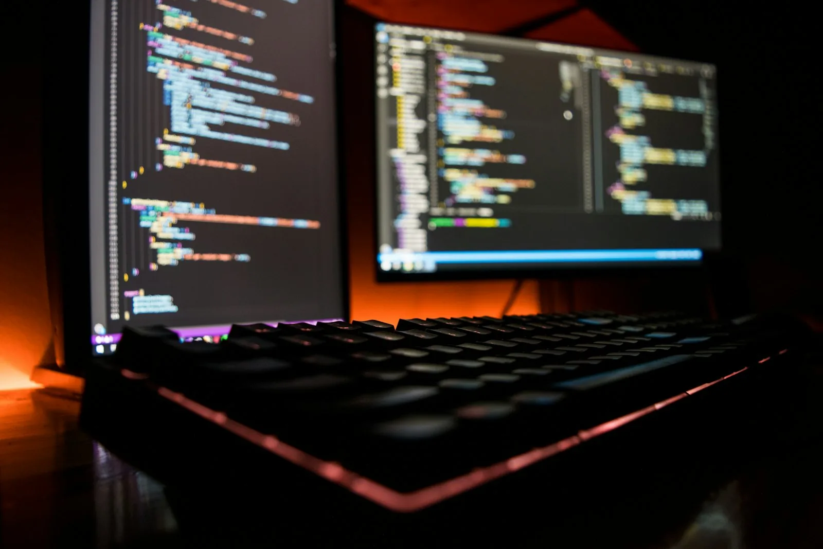 A backlit mechanical keyboard in front of two dark code editors, mid-session